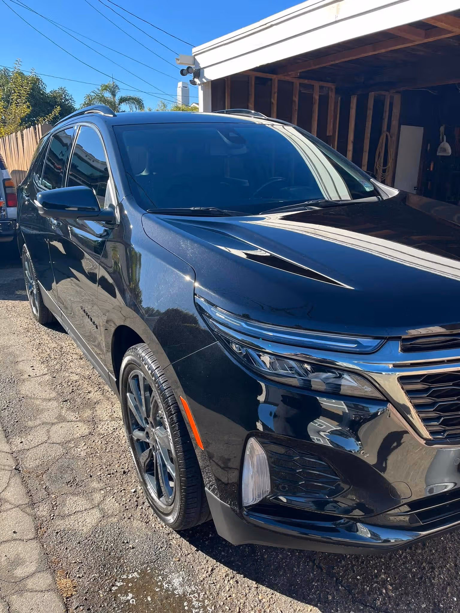 Black SUV parked outside on a sunny day near a wooden fence and garage structure.