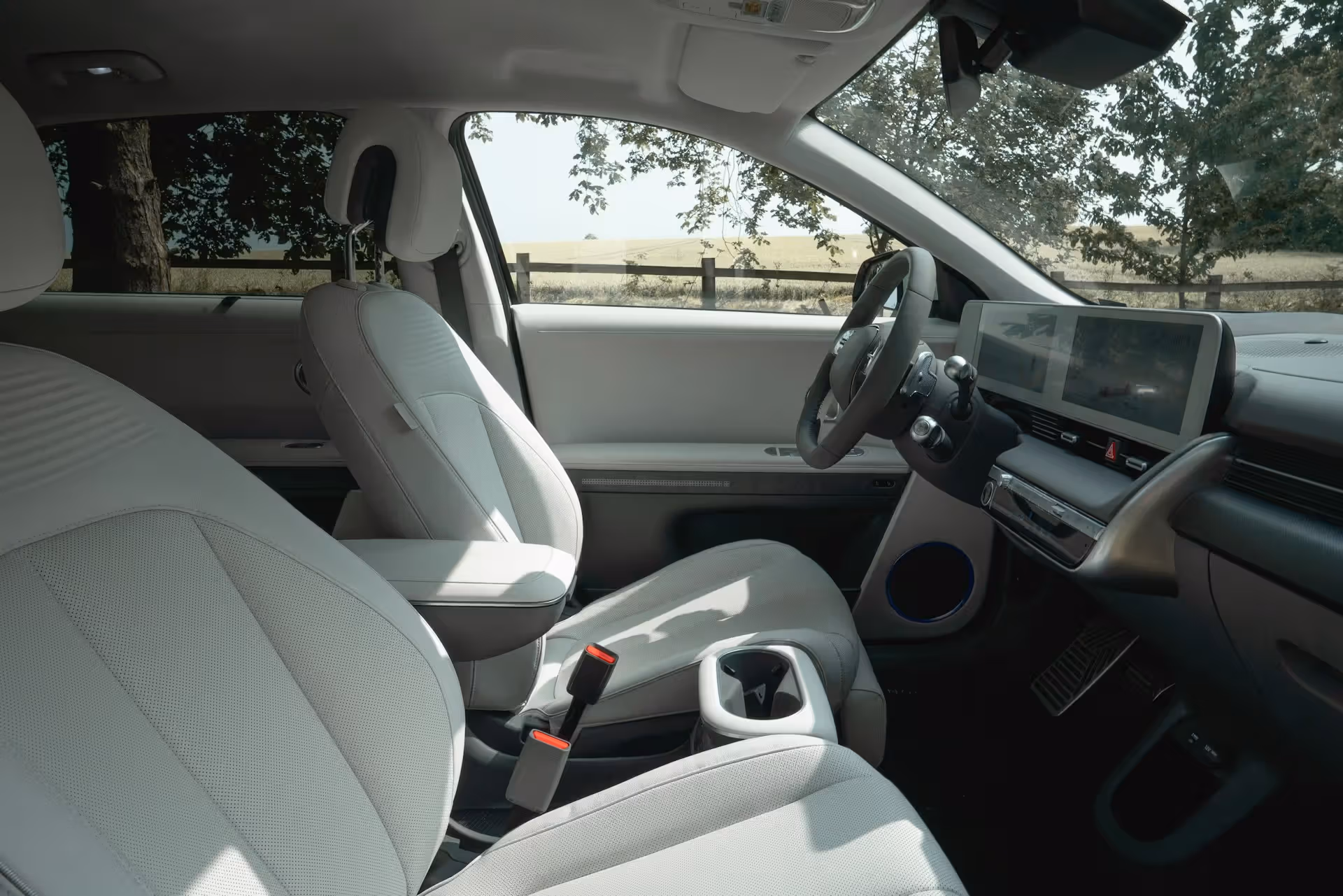 Interior of a modern car with white seats, digital dashboard, and steering wheel with outdoor view.