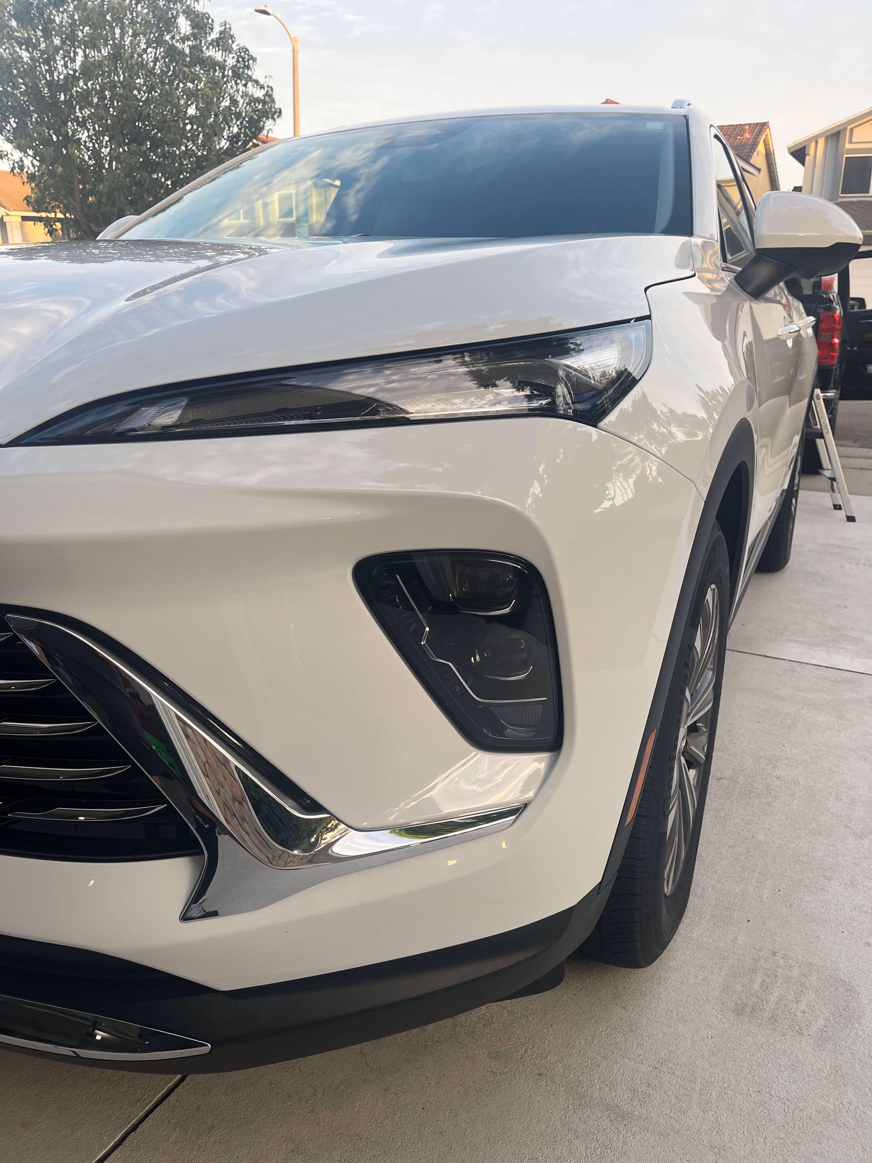 Front side view of a white SUV parked on a concrete driveway with reflections on its hood and windows.