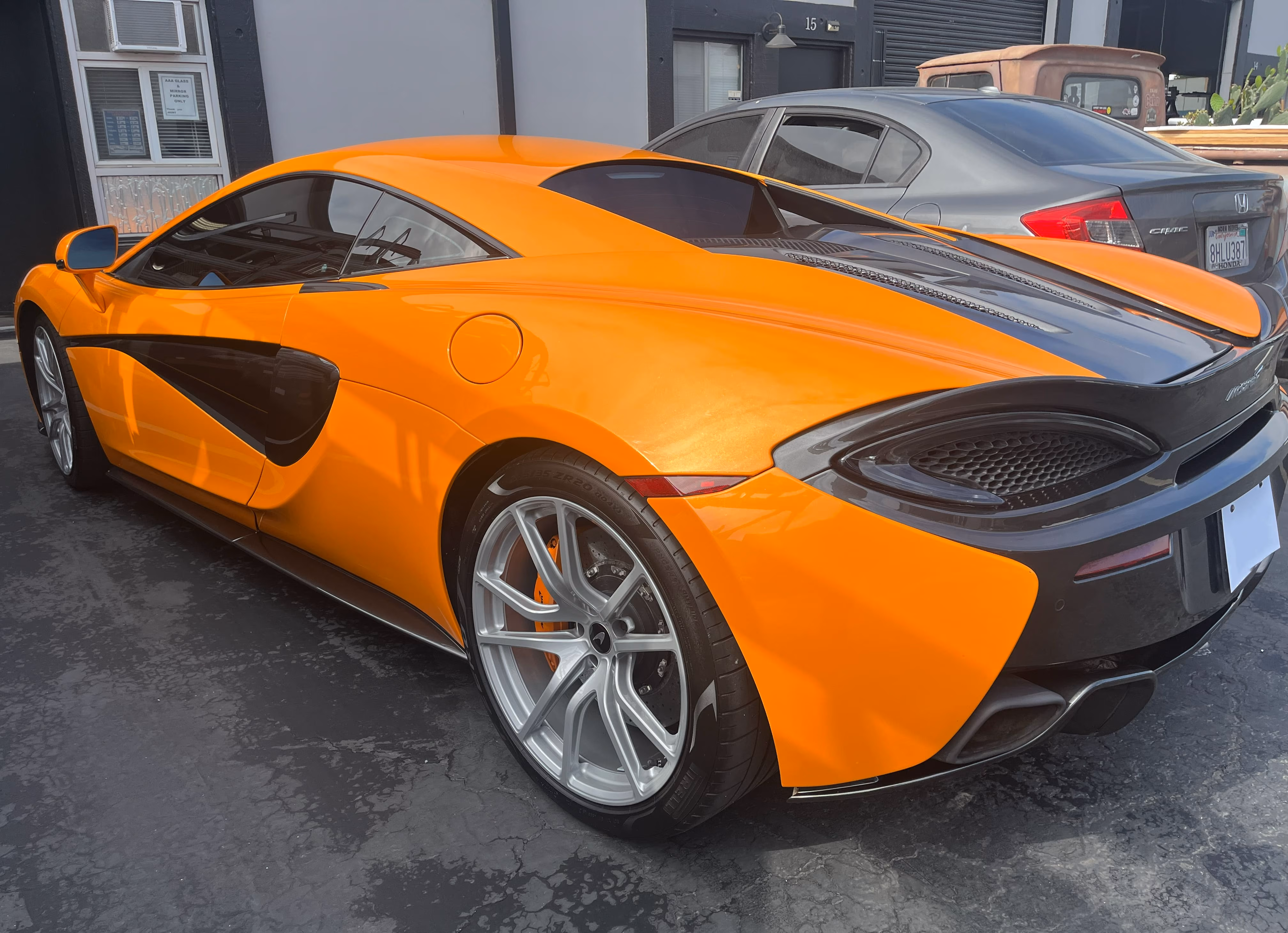 Orange McLaren sports car with black accents parked next to a gray Honda Civic on asphalt.