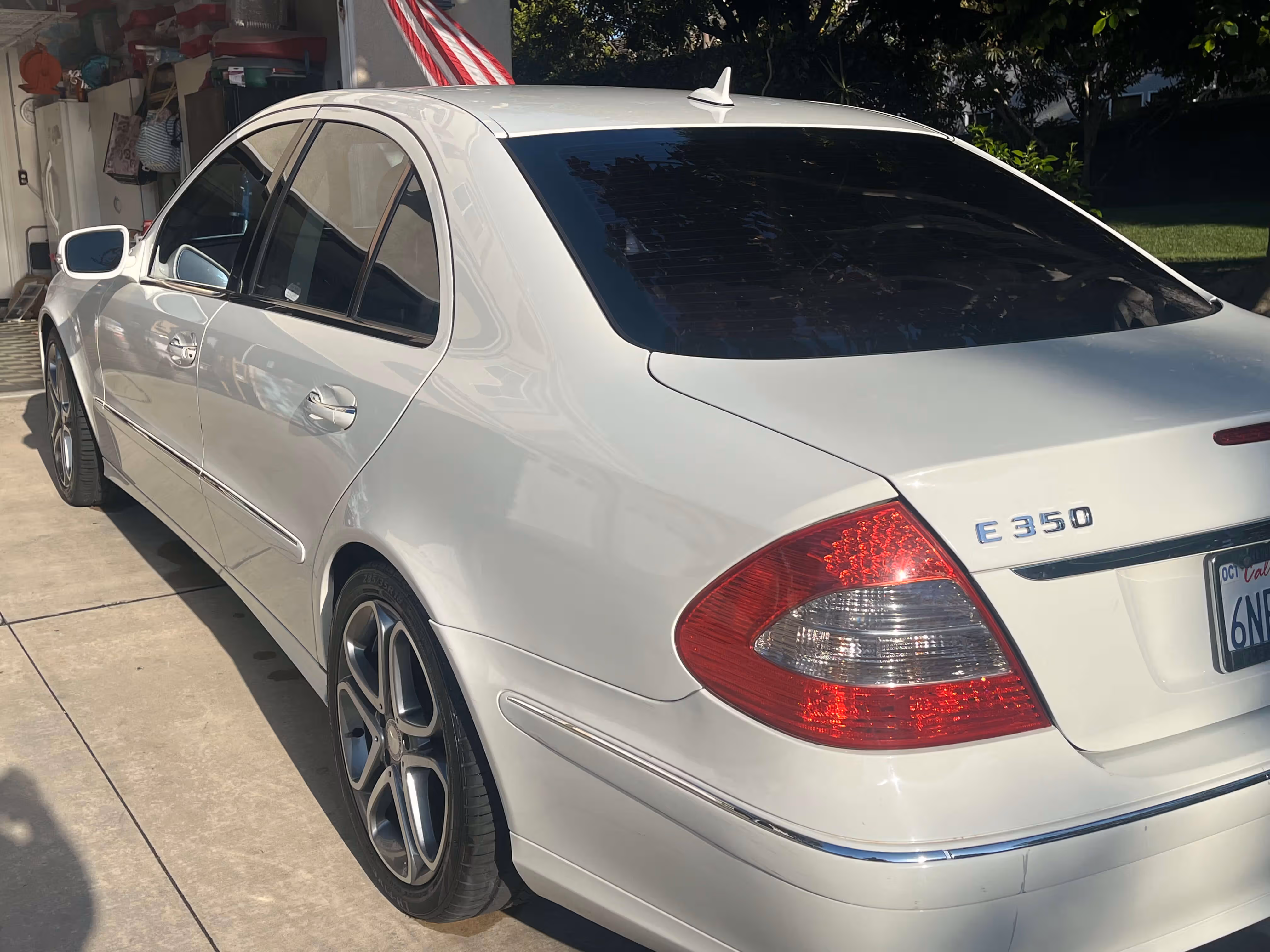 White Mercedes-Benz E350 sedan parked in a driveway under sunlight with tinted windows.