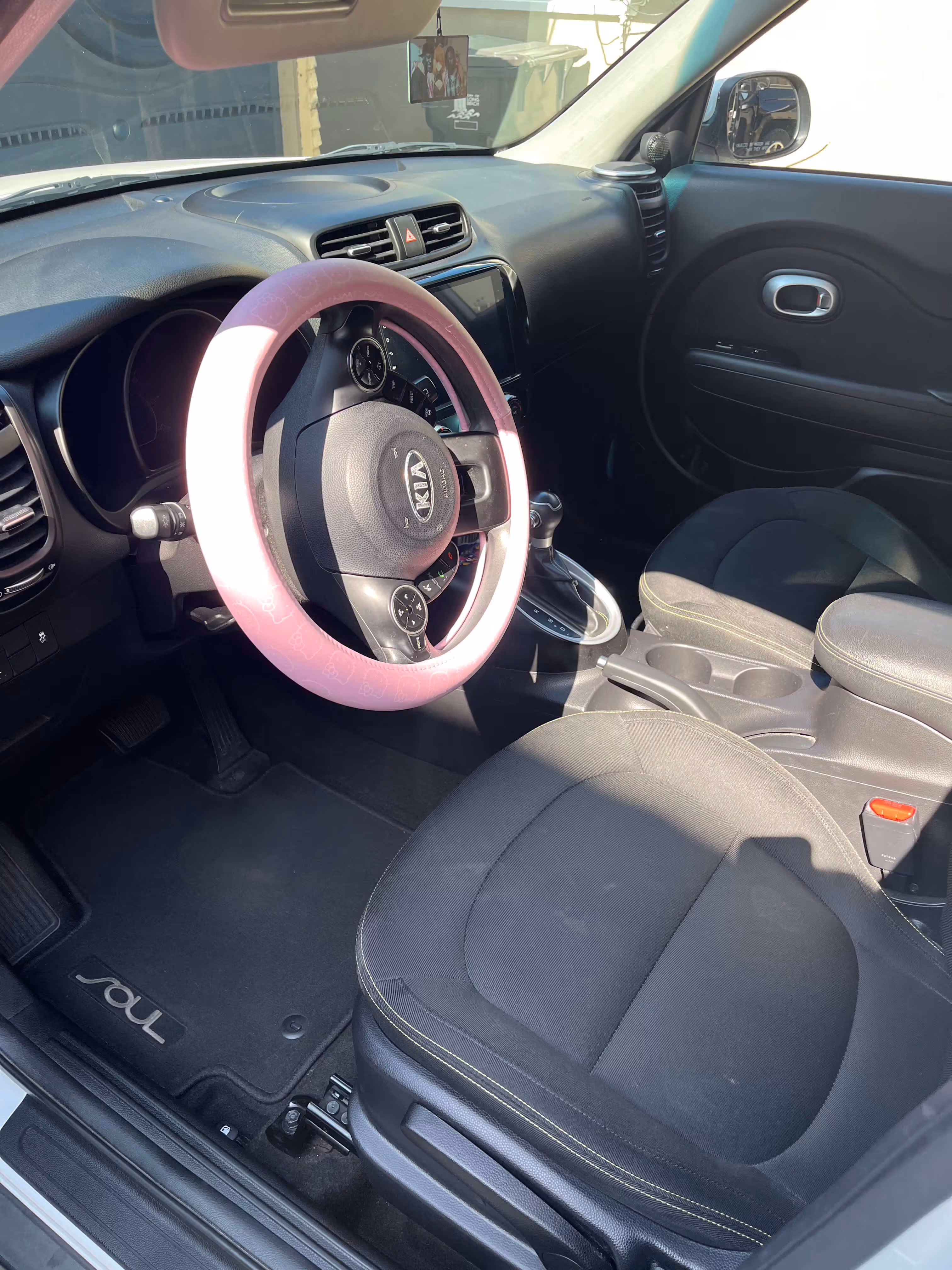 Interior of Kia Soul car showing steering wheel with pink cover and black front seats.