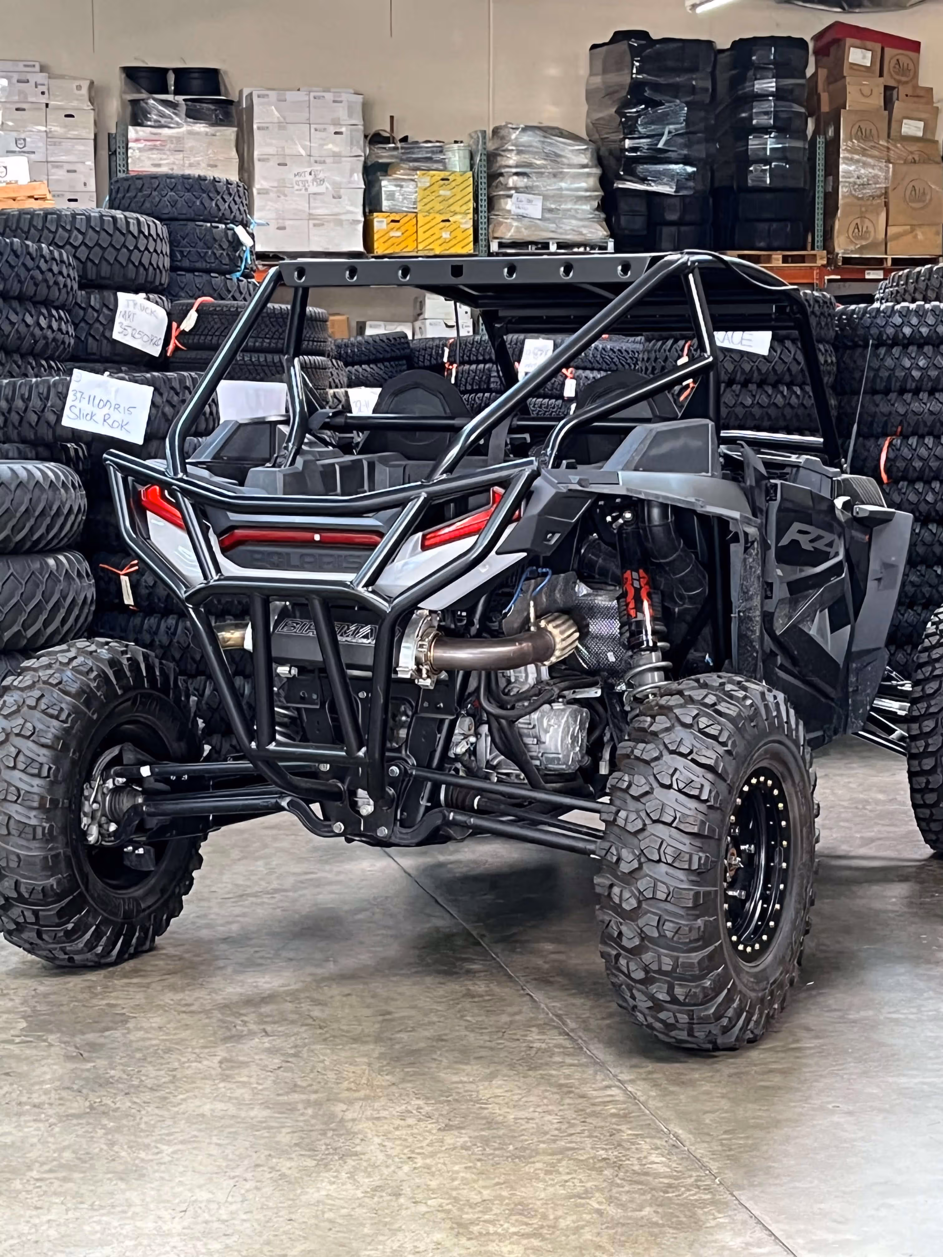 Black Polaris off-road vehicle with rugged tires inside a warehouse stacked with tires and boxes.