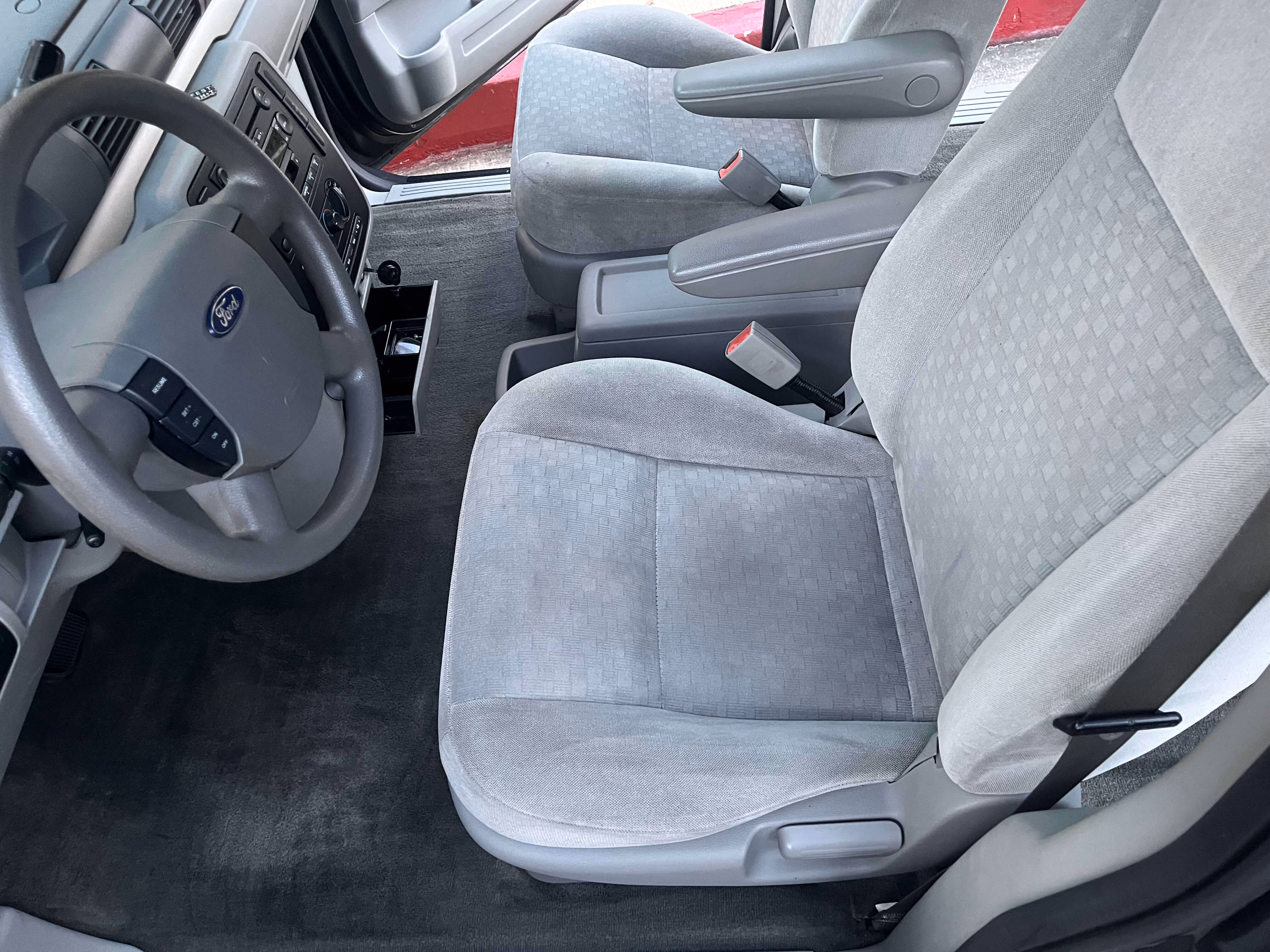 Interior of a car showing gray fabric front seats, a steering wheel with Ford logo, and carpeted floor.