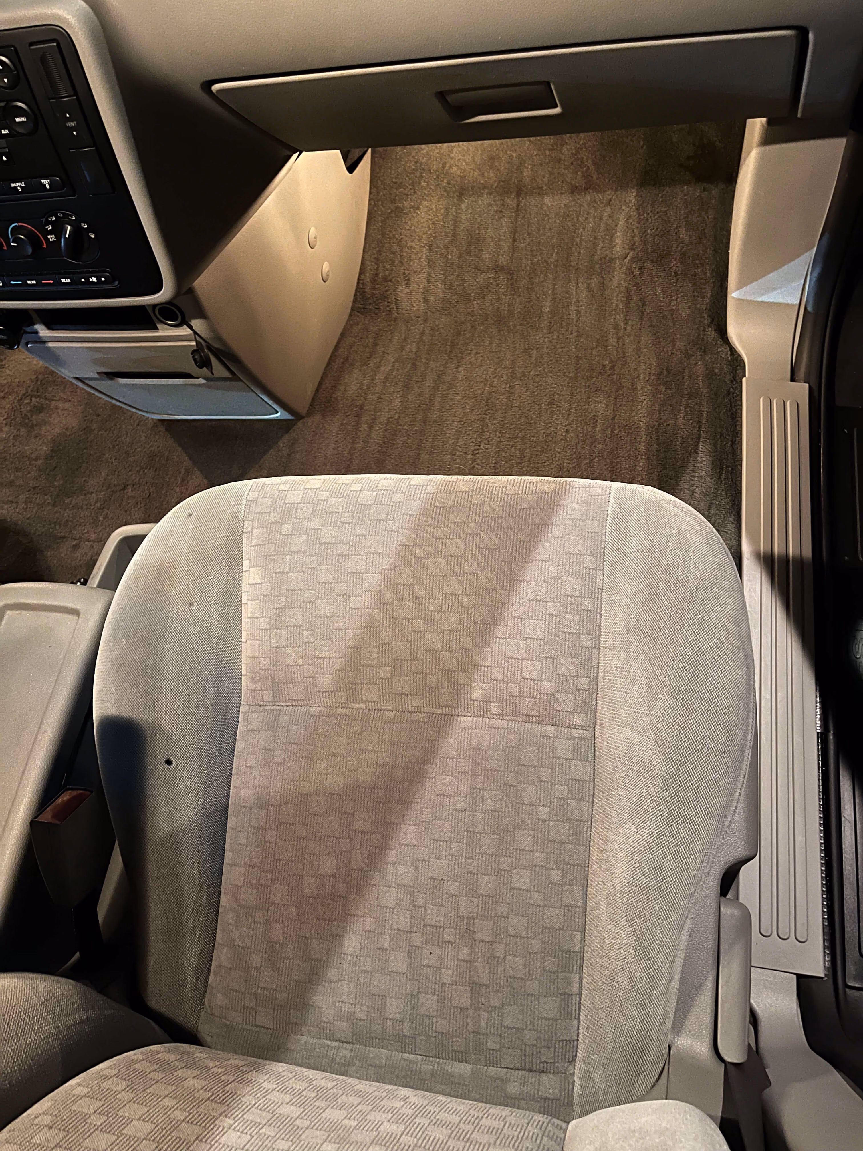 Clean gray fabric car seat with patterned upholstery and beige interior floor and dashboard area.