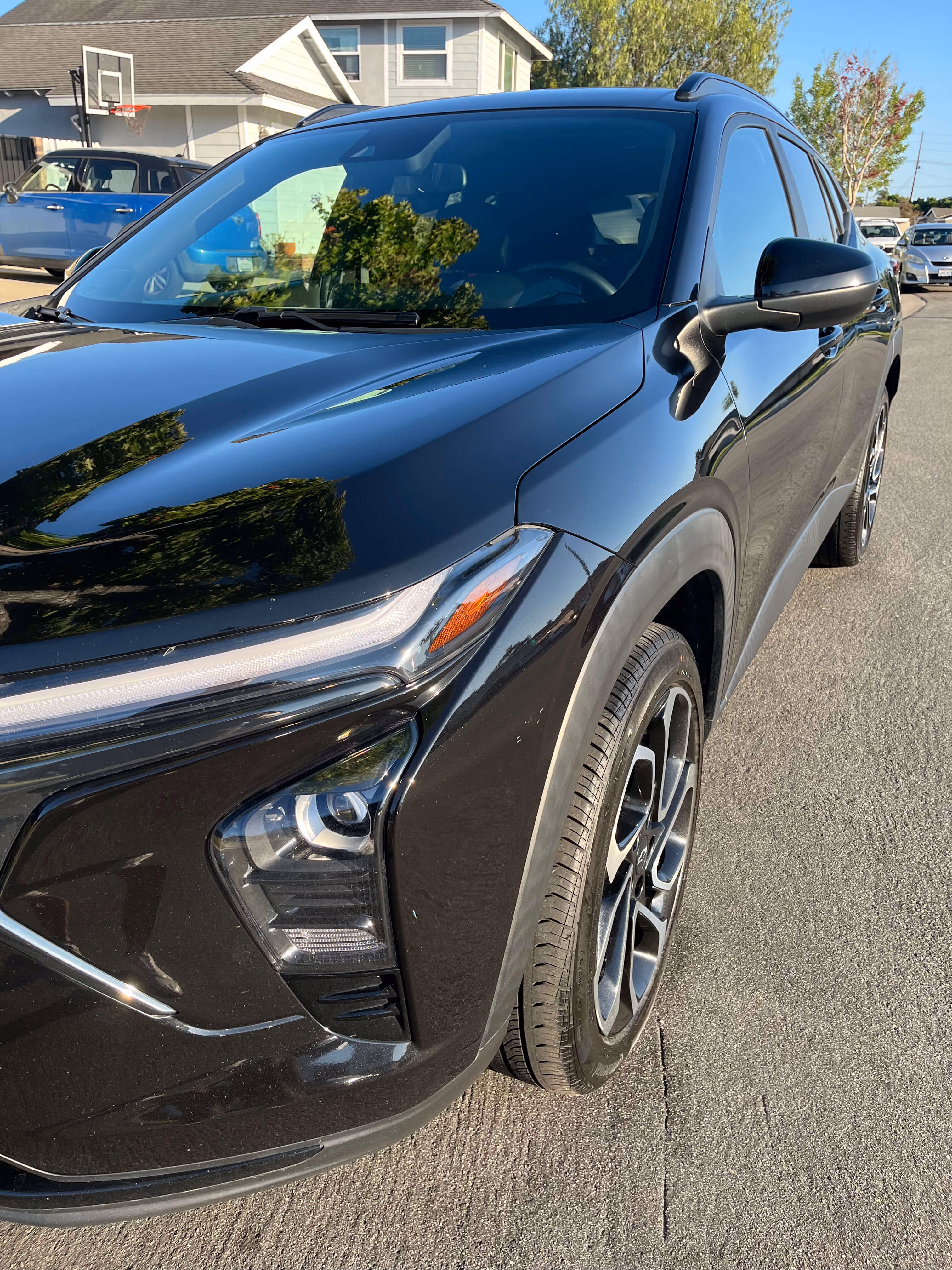Close-up of a black SUV's front left side, showing the headlight, side mirror, and wheel on a street.