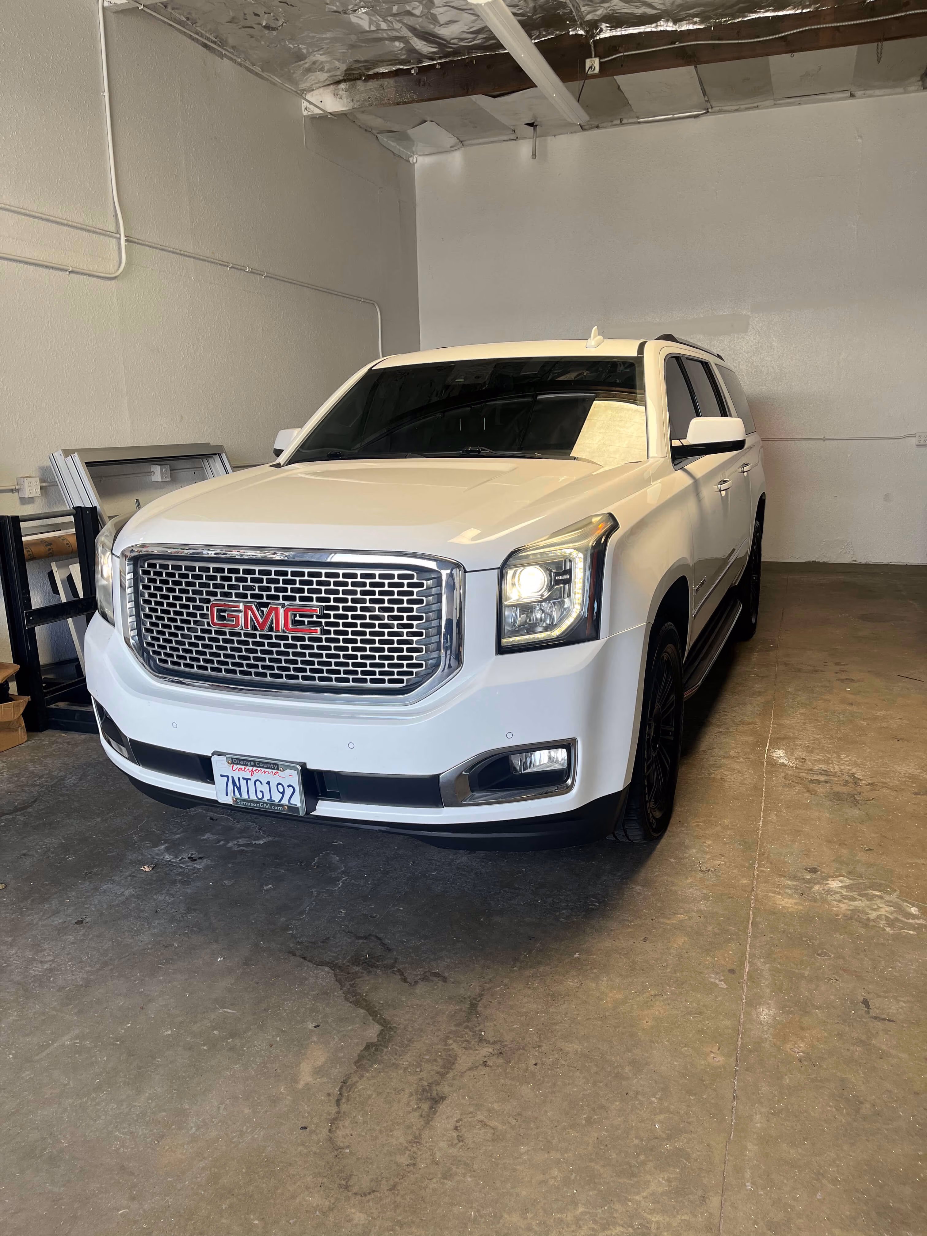 White GMC SUV parked indoors on a concrete floor with front lights on.