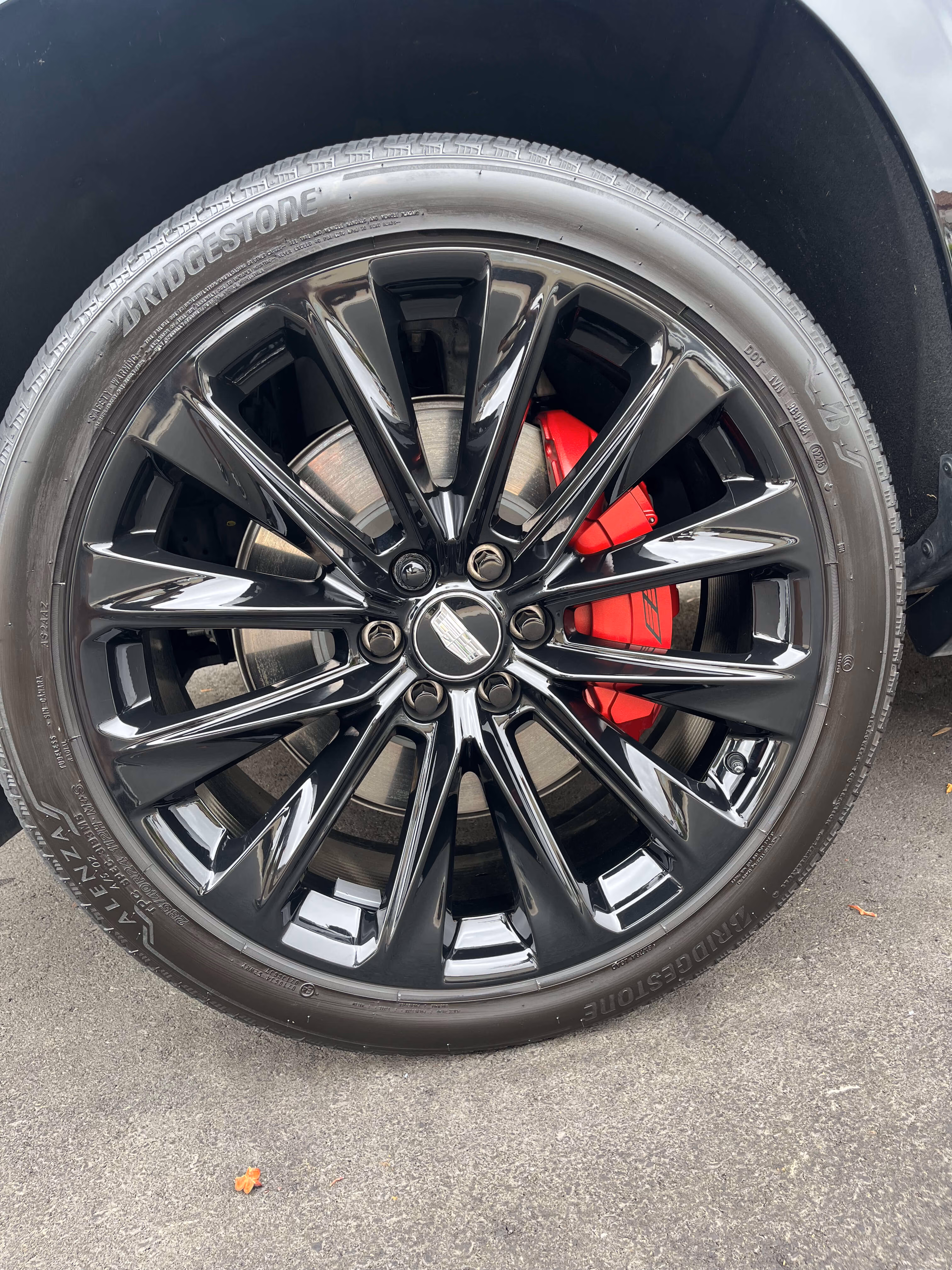 Close-up of a black multi-spoke car wheel with a red brake caliper and Bridgestone tire.