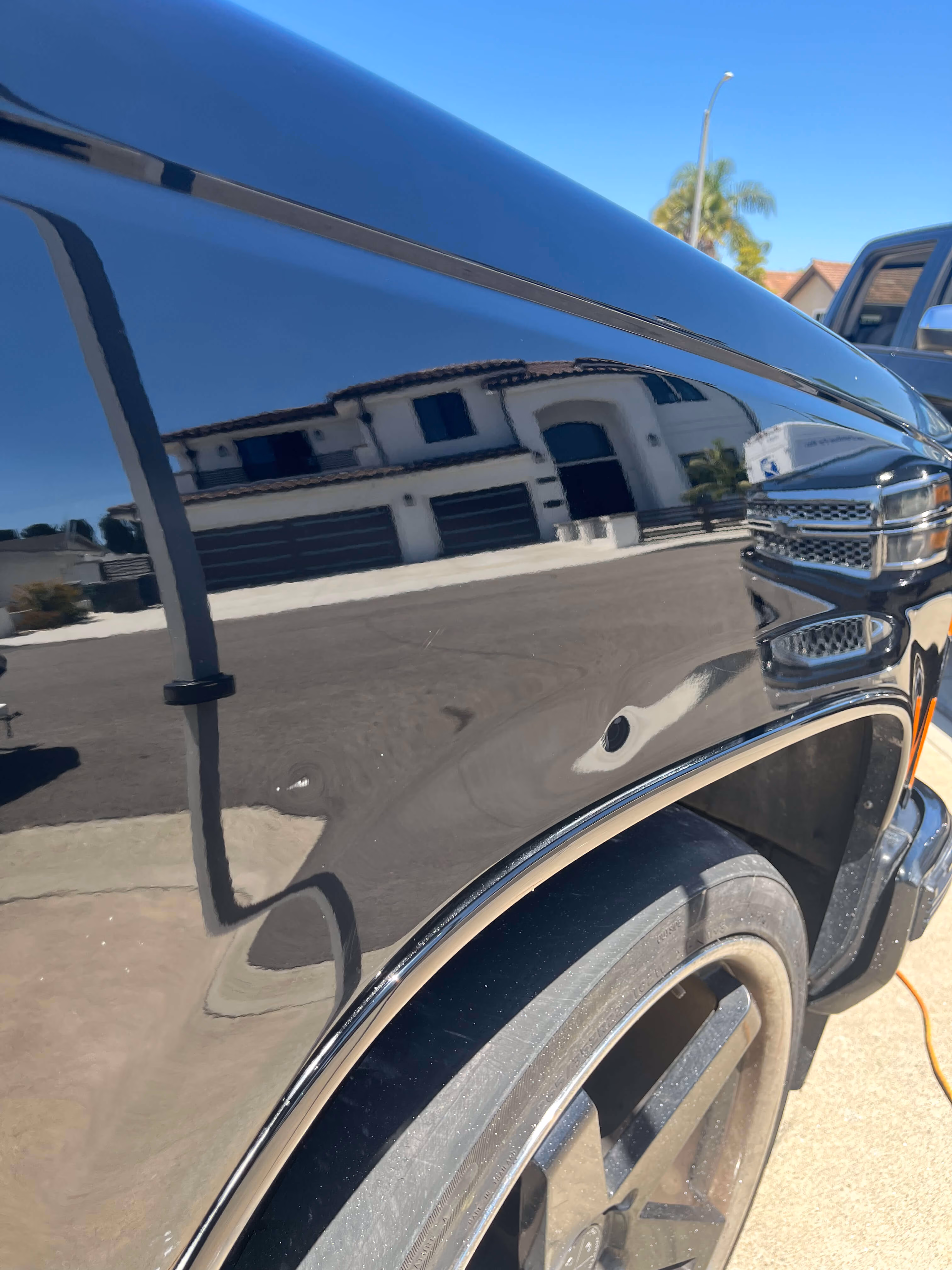 Reflection of a house and street visible on the shiny black surface of a vehicle's fender near a wheel.
