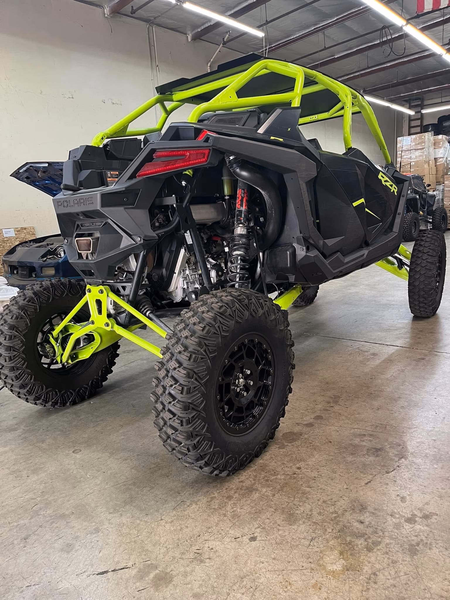 Black and neon green Polaris RZR off-road vehicle with large rugged tires parked indoors.