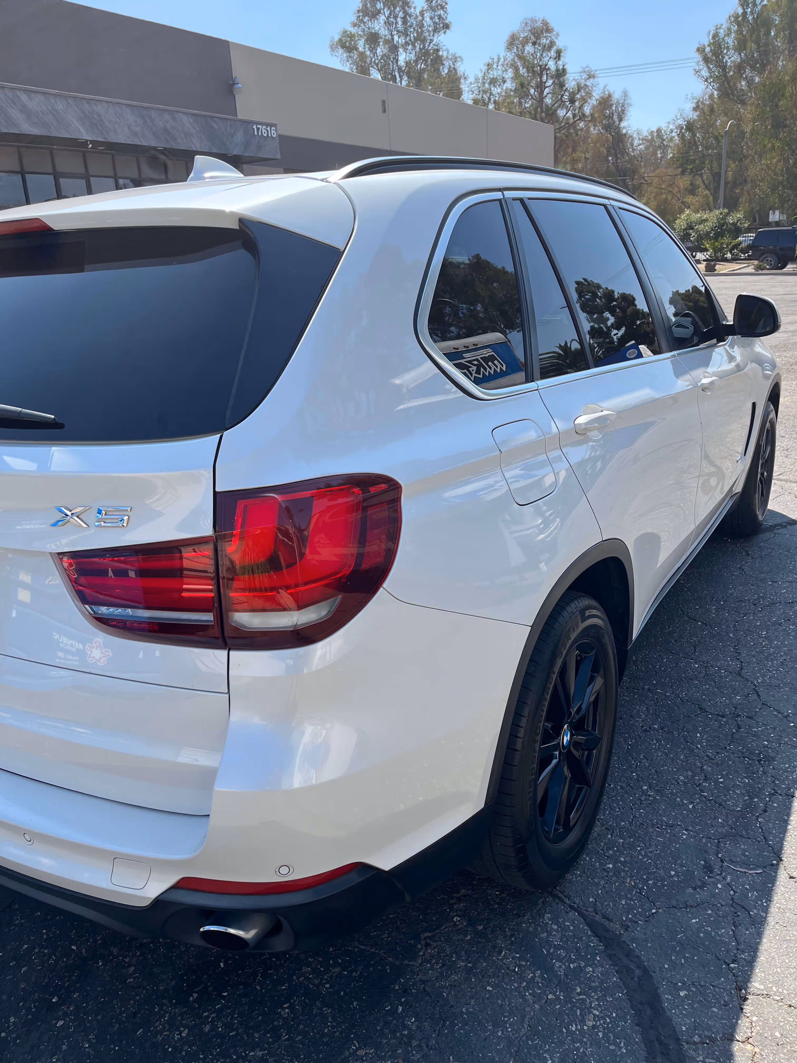 Rear side view of a white BMW X5 SUV parked on a cracked asphalt surface.
