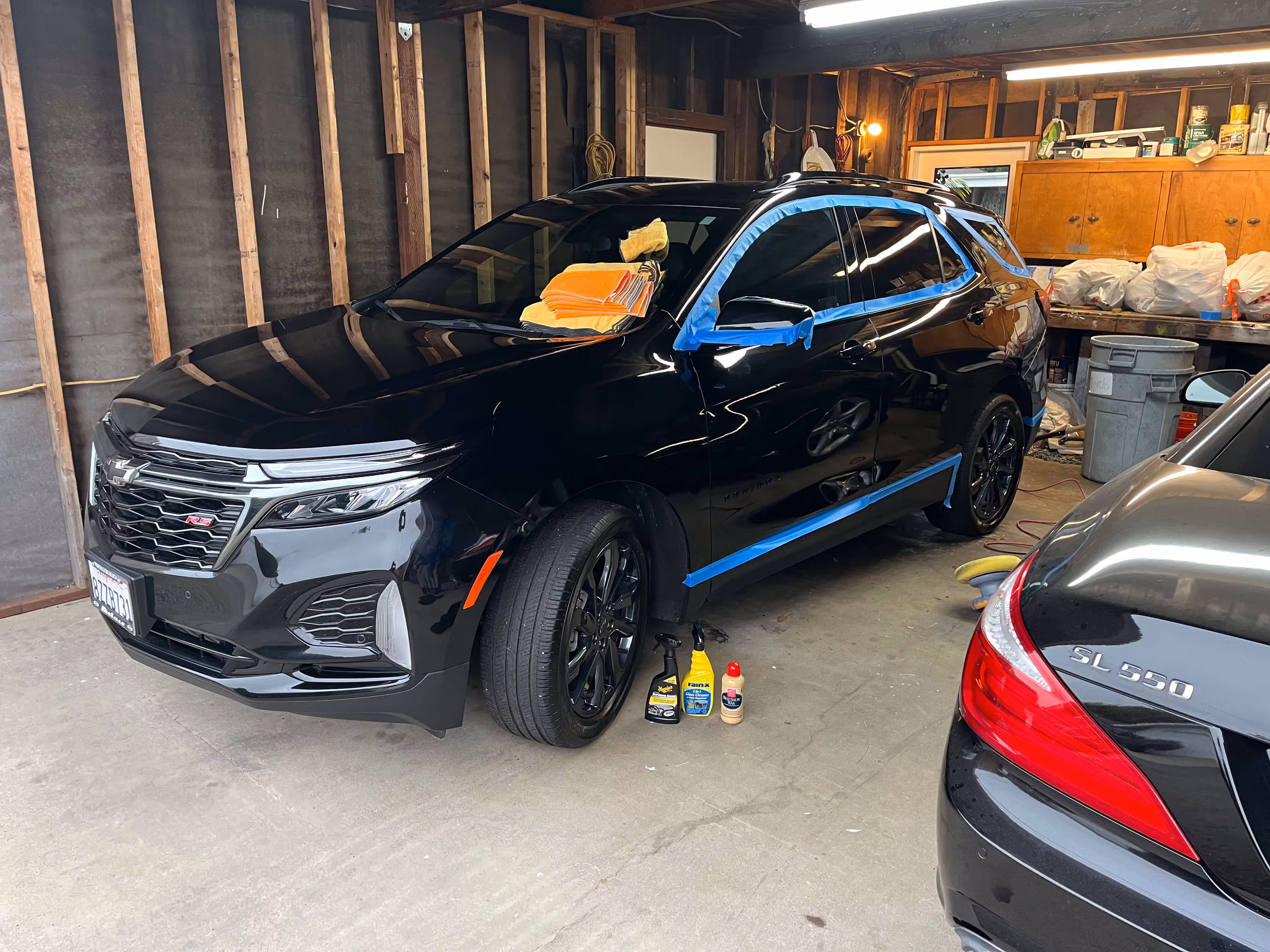 Black Chevrolet SUV being detailed in a garage with cleaning supplies and microfiber towels on it.